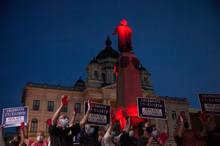 A crowd of about 200 people gathered at Columbus Circle in Syracuse to hear speakers advocate for the removal of the colonizer’s statue on Indigenous Peoples’ Day in October. At the end of the event, organizers announced a minute of silence where attendees raised gloved hands and signs in front of the Columbus statue, illuminated in red light, to indicate he had blood on his hands.